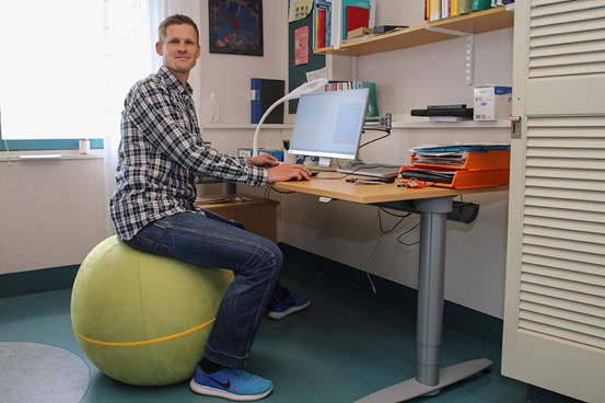 Daniel Carlsson sitter på en stor boll vid ett skrivbord där det står en dator.