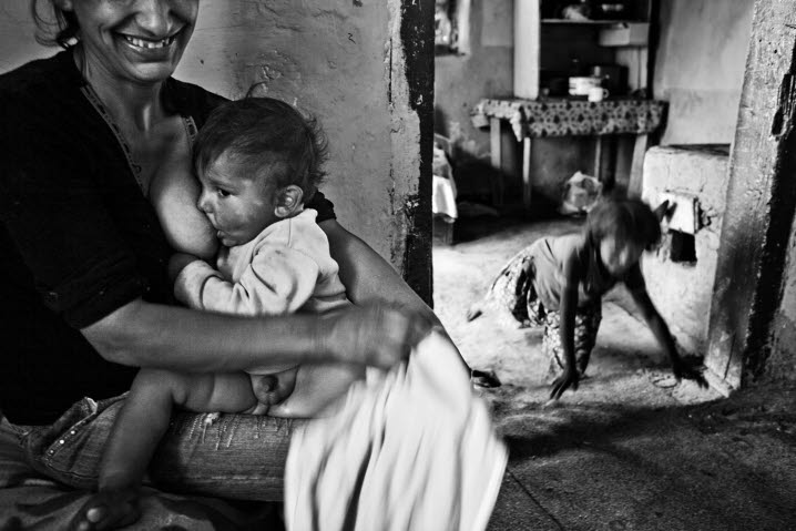 Åke Ericsons svartvita fotografi av romsk interiör i Rumänien. En mamma ammar i förgrunden sitt barn, i dörröppningen bakom ses ett annat barn i rörelse.