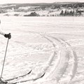 Person på skidor vid ett skoterspår på en sjö och en liten by med en kyrka i bakgrunden.