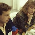 Personer i 80-talsfrisyrer framför en dator.
