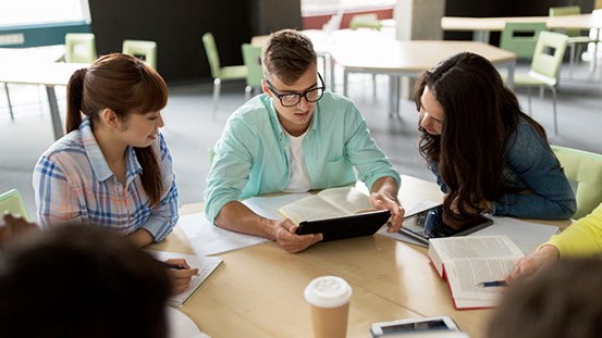 Studenter sitter runt ett bord och studerar tillsammans.