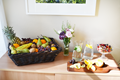 Bord med en en fruktkorg, blomvas, vattenkaraffer och uppskuren apelsin på en skärbräda.