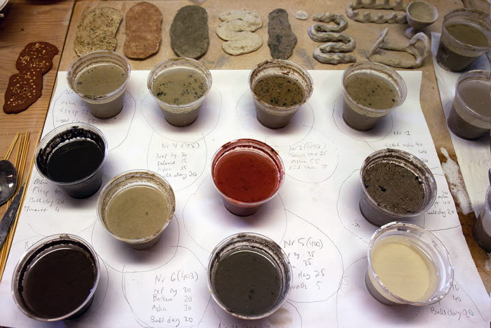 Burkar med glasyrprover i olika färger står uppradade på ett bord. Här har bland annat aska blandats med lera och vatten och fungerar som en slags glasyr.