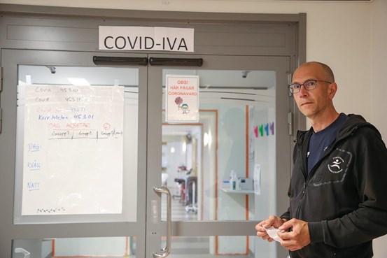 Jonas Bolin i halvfigur, står utanför en stängd glasdörr. På en skylt ovanför dörren står det Covid IVA.