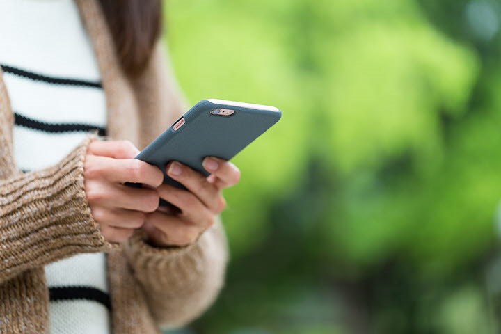 En kvinna står och knappar på en mobiltelefon.