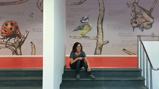 KLARTTEXT: Konstnären Ida Rödén sitter på trappan framför hennes väggmålning med djur på Wendela Hellmanskolan i Härnösand.