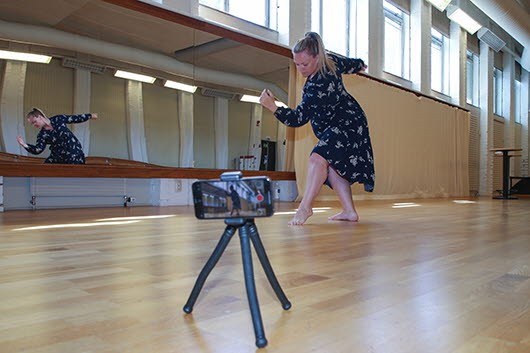 Martha Widén dansar i en gymnastiksal. En mobilkamera i stativ står i förgrunden.