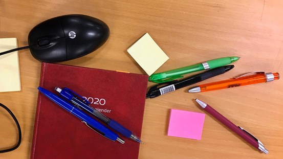 Skrivbordsyta med kalender, pennor, papper och datormus.
