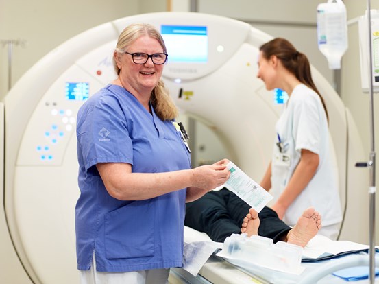 Två sjuksköterskor som hjälper en patient som förbereds för röntgenundersökning.