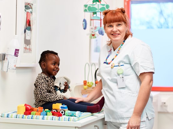 Sjuksköterska står framför ett skötbord och håller ena handen på en lite pojke sitter och håller i en leksak.