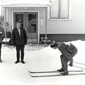 Personer framför entrén på ett hus varav en har en nummerlapp och tävlar i skidåkning.