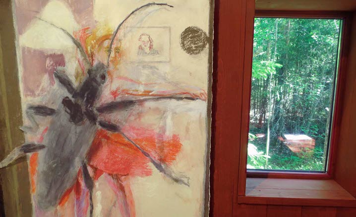 På en vägg inne i Konstbiotopens hus syns detaljen av en målning där en stor skalbagge kryper på ett fönster så att den tycks dansa med en flicka i röd kjol. Till höger om målningen ses skogen genom ett av husets fönster. 