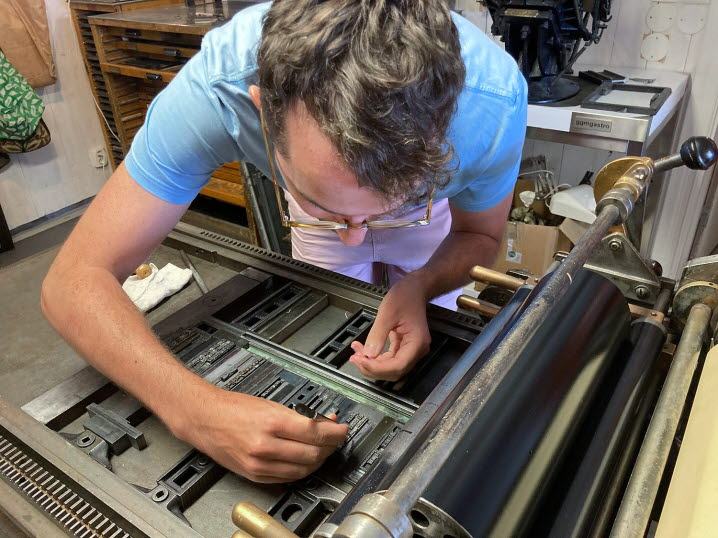 En deltagare i Tomma Rum står lutad över tryckpressen och justerar några bokstäver.