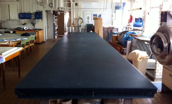 Foto: Ett långt tryckbord sträcker sig från betraktaren in i rummet. Bordsytan är svart.