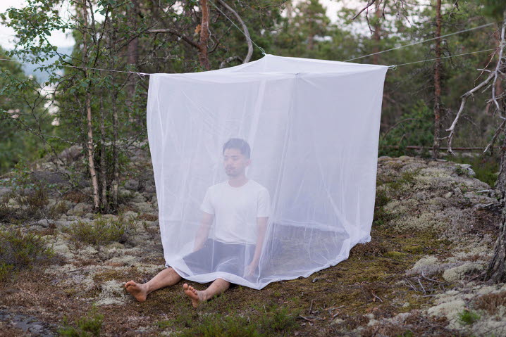 Fotografi som visar Suchart Wannaset sittandes inuti ett moskitnät rest på ett berg, med benen utanför nätet så att myggen kan sticka.