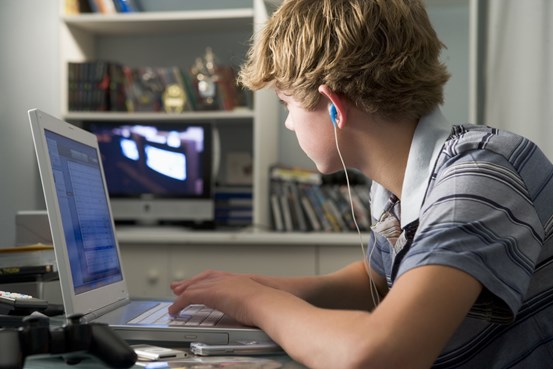 Pojke sitter framför en bärbar dator med hörlurar i öronen
