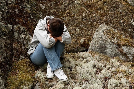 Ung person sitter hopkrupen på en mossklädd sten, huvudet nedböjt