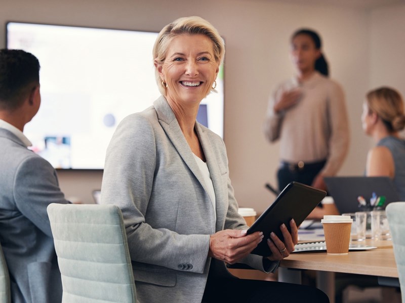 Kvinnlig företagare i mötesrum, med läsplatta i handen, tittar leende rakt in i kameran
