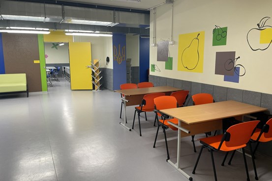 Klassrum i en underjordisk skola med bord, orange stolar och färgglada väggdekorationer.