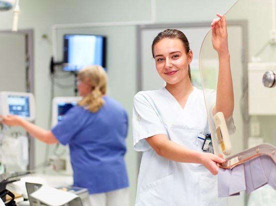 Tandsköterska i ett behandlingsrum, suddig bakgrund där en tandläkare behandlar en patient.