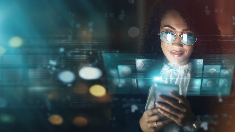 Person använder en mobil framför en digital skärm med futuristiska ljuseffekter och flera informationsrutor som illustrerar avancerad teknik och AI‑utveckling.