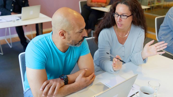 Personer arbetar tillsammans vid ett bord i en utbildningssituation, med laptop, anteckningar och kursmaterial framför sig.