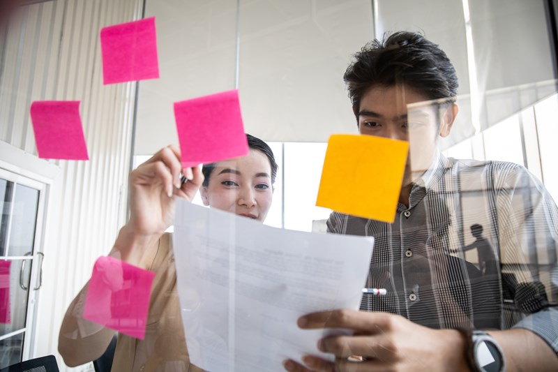 Företagare som sätter upp post-it på en genomskinlig tavla