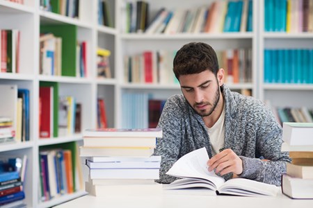 En kille sitter i ett bibliotek och bläddrar i en bok.