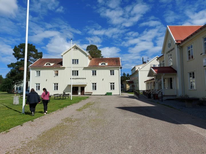 Hola folkhögskolas ena skolbyggnad, en blå himmel och två personer som går över en grusplan framför byggnaden.
