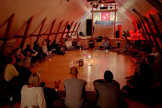 En grupp personer sitter i en cirkel med levande ljus i mitten och lyssnar till en ledare som pratar.