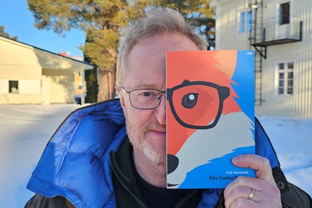 En man står utomhus och håller upp en bok med en räv på framför halva ansiktet.