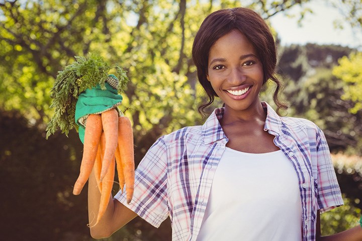En kvinna håller upp ett knippe morötter och ler in i kameran.