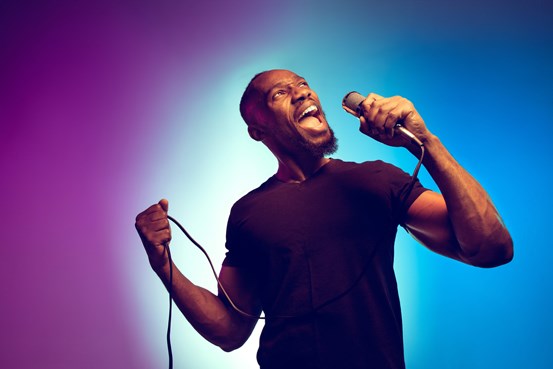 En man står och sjunger i en mikrofon framför en blå och lila bakgrund.