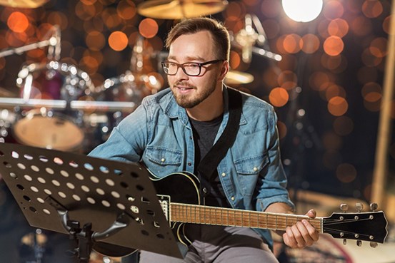 En man sitter med en gitarr och läser noter i en studio.