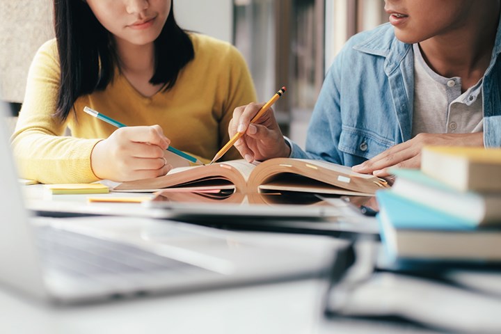 Två studenter sitter och studerar tillsammans med böcker.