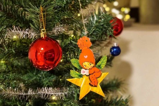 Närbild på en julgran med några röda kulor och en dekoration i papper med en stjärna och en tomte.