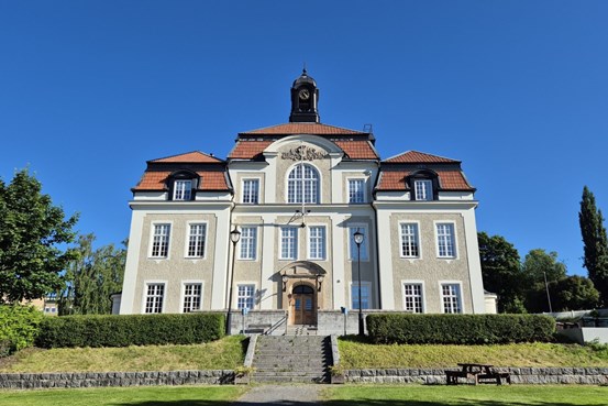 Örnsköldsviks folkhögskola framifrån med blå himmer och grönt i parken nedanför.