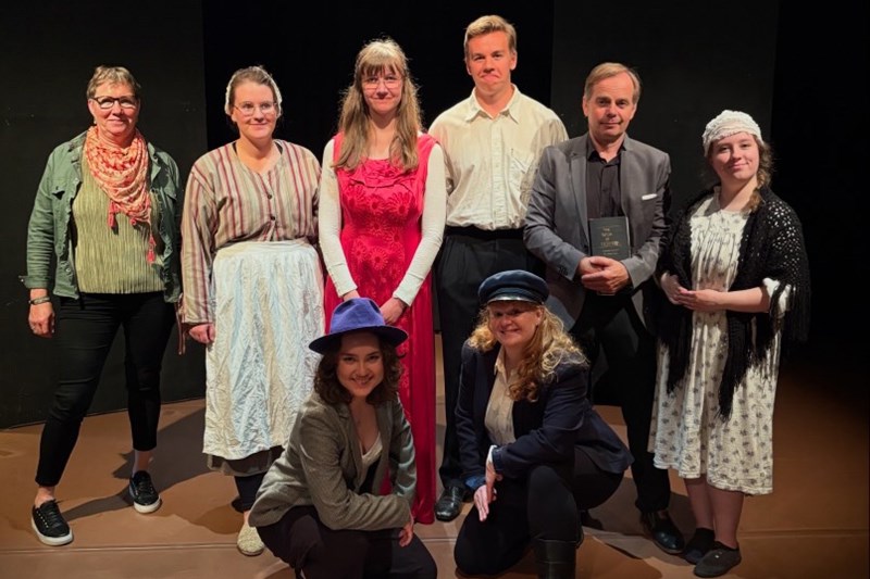  En grupp deltagare i teaterkostymer på en gruppbild bredvid skolans rektor.