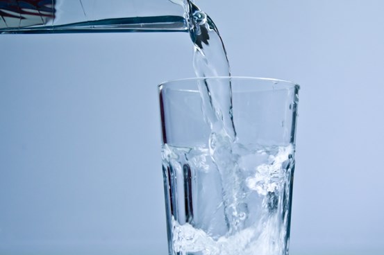 Ett glas fylls med vatten med hjälp av en kanna.