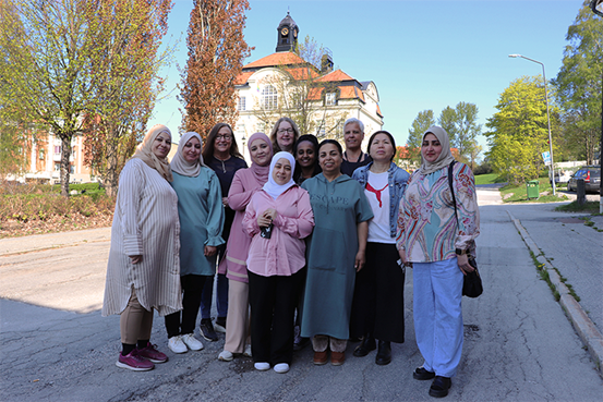 En grupp deltagare och personal står uppradade för en gruppbild utomhus med skolans huvudbyggnad i bakgrunden.