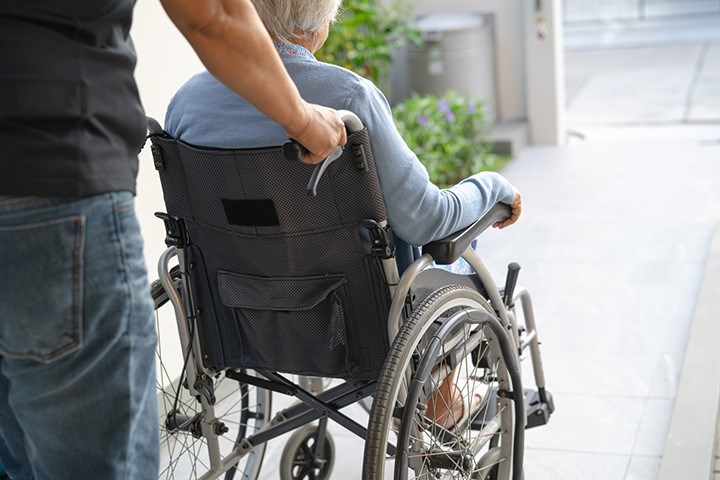 En person styr en äldre person som sitter i rullstol