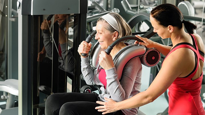 En yngre kvinna hjälper en äldre kvinna med en träningsmaskin i ett gym