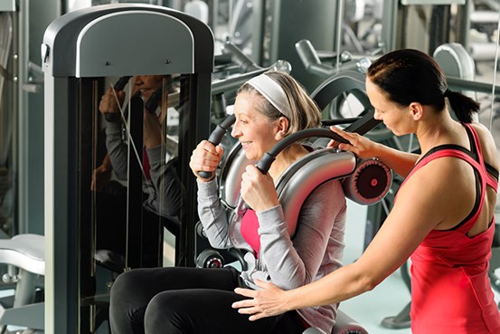 En yngre kvinna hjälper en äldra kvinne med en träningsmaskin på ett gym