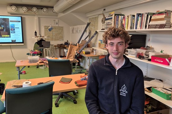 En ung man sitter i ett klassrum och tittar in i kameran. 