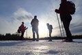 Fyra personer fotade lite underifrån står med skidutrustning och packning i ett öppet vinterlandskap.