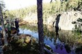 Några personer som vandrar i skogen intill ett vattendrag i en bergsskreva.