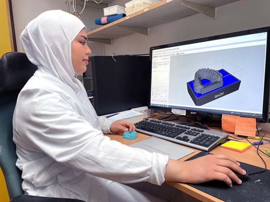Tandtekniker Shahd sitter vid en dator som visar en tandmodell på skärmen.