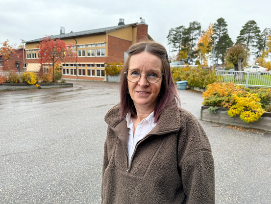 Kvinnlig rektor står utanför en skola utomhus en höstdag.