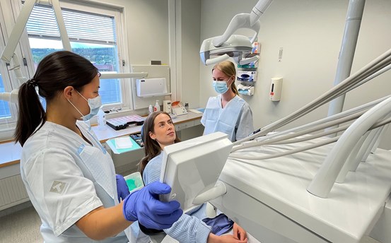 Tre tandläkarstuderande arbetar i ett behandlingsrum, en av dem låtsas vara patient.