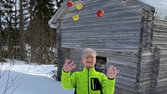 Helene Andersson står utomhus hemma vid företaget och jonglerar med äpplen.